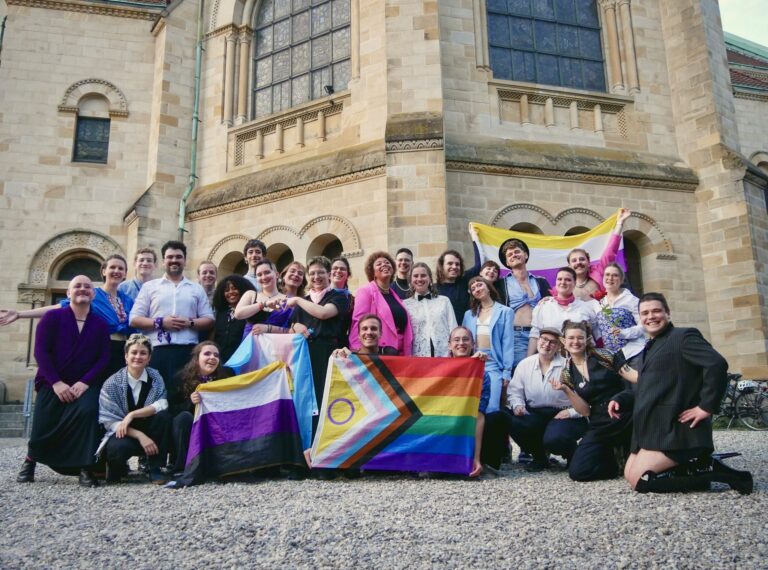 Das queerchor vor der Pauluskirche Basel im Gruppenbild mit Pride-Flaggen